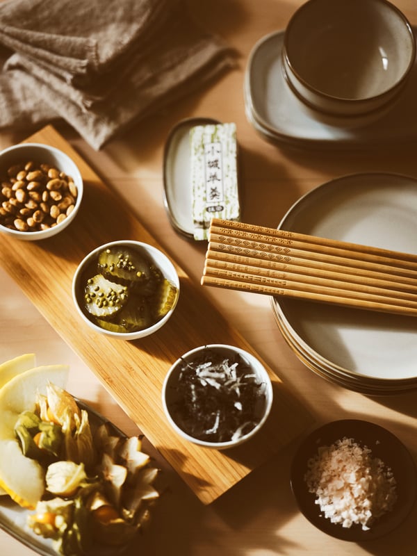 TREBENT chopsticks on a GLADELIG side plate, a bamboo/white TYNGDLÖS tray with 3 bowls set, and side plates set on a table.