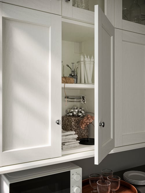 A modern kitchen featuring a wall cabinet with two doors, a side plate, a jar, and an unscented chandelier candle.