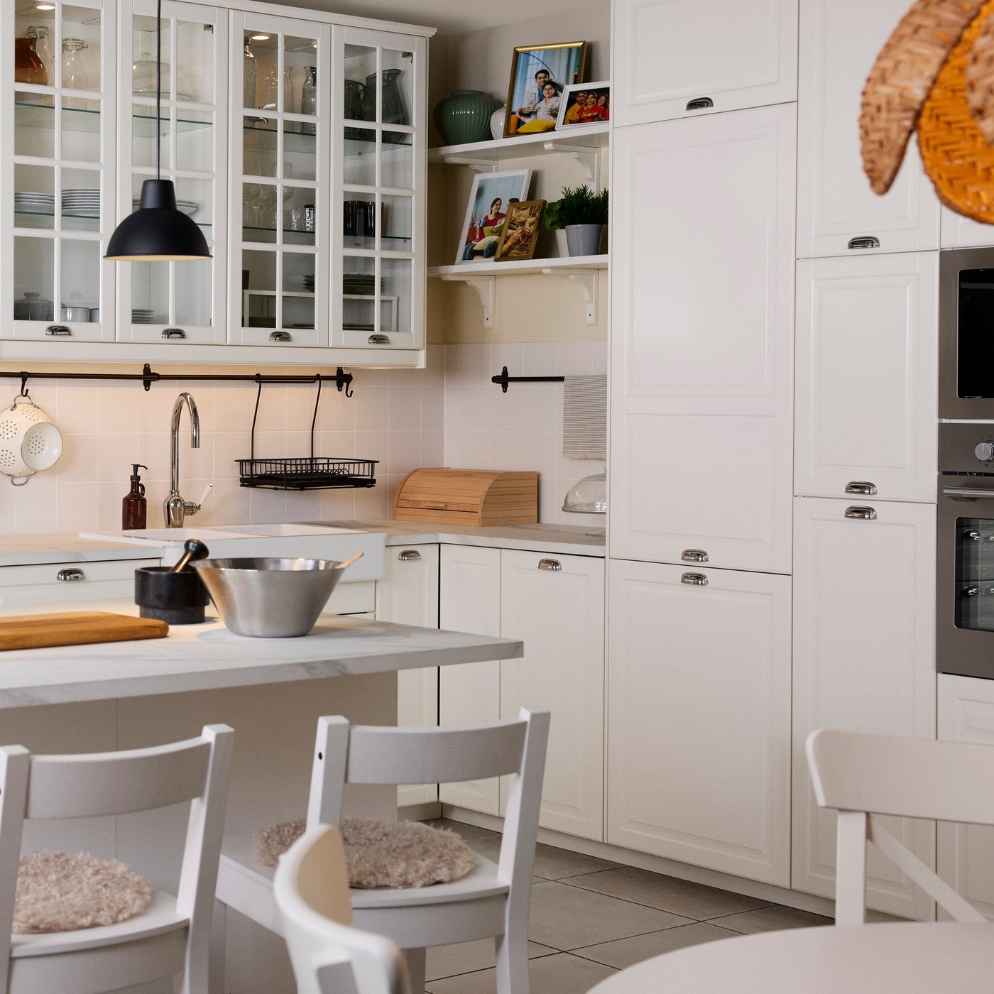 A bright kitchen has white traditional BODBYN fronts and a kitchen island with a dining table in front.