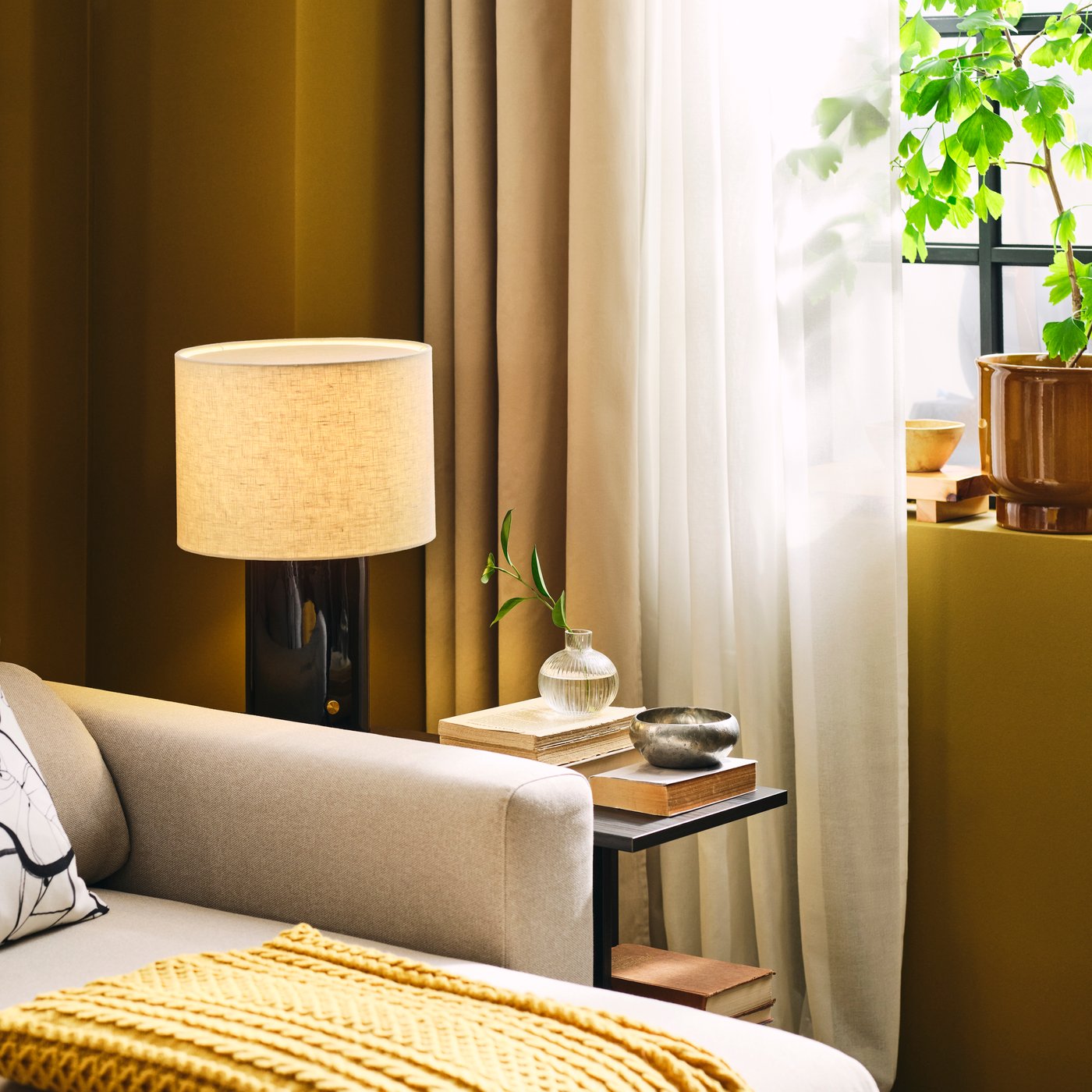 Dans le salon, on trouve un canapé MALMKÖPING 3 places de couleur beige clair avec méridienne, placé à côté d'une plante et de lampes.