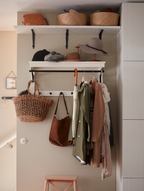 Hallway with white hat rack on the wall, clothes and hats placed on the knobs, wall shelf, three baskets, wooden stepladder.