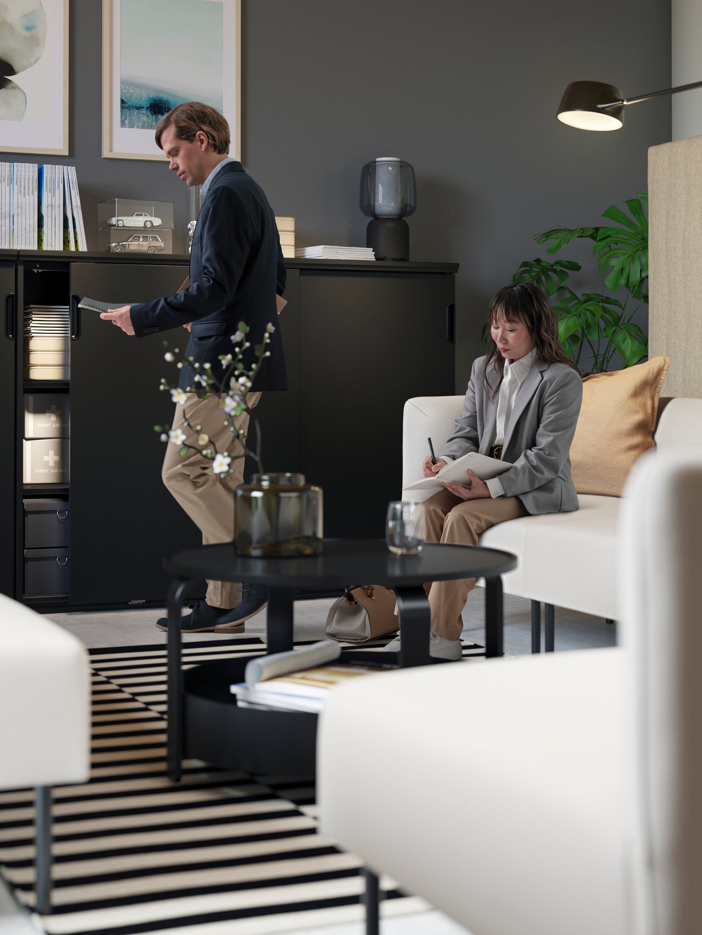A lounge area with LILLEHEM beige modules, a black round BORGEBY coffee table and GALANT storage. A man and a woman are working.