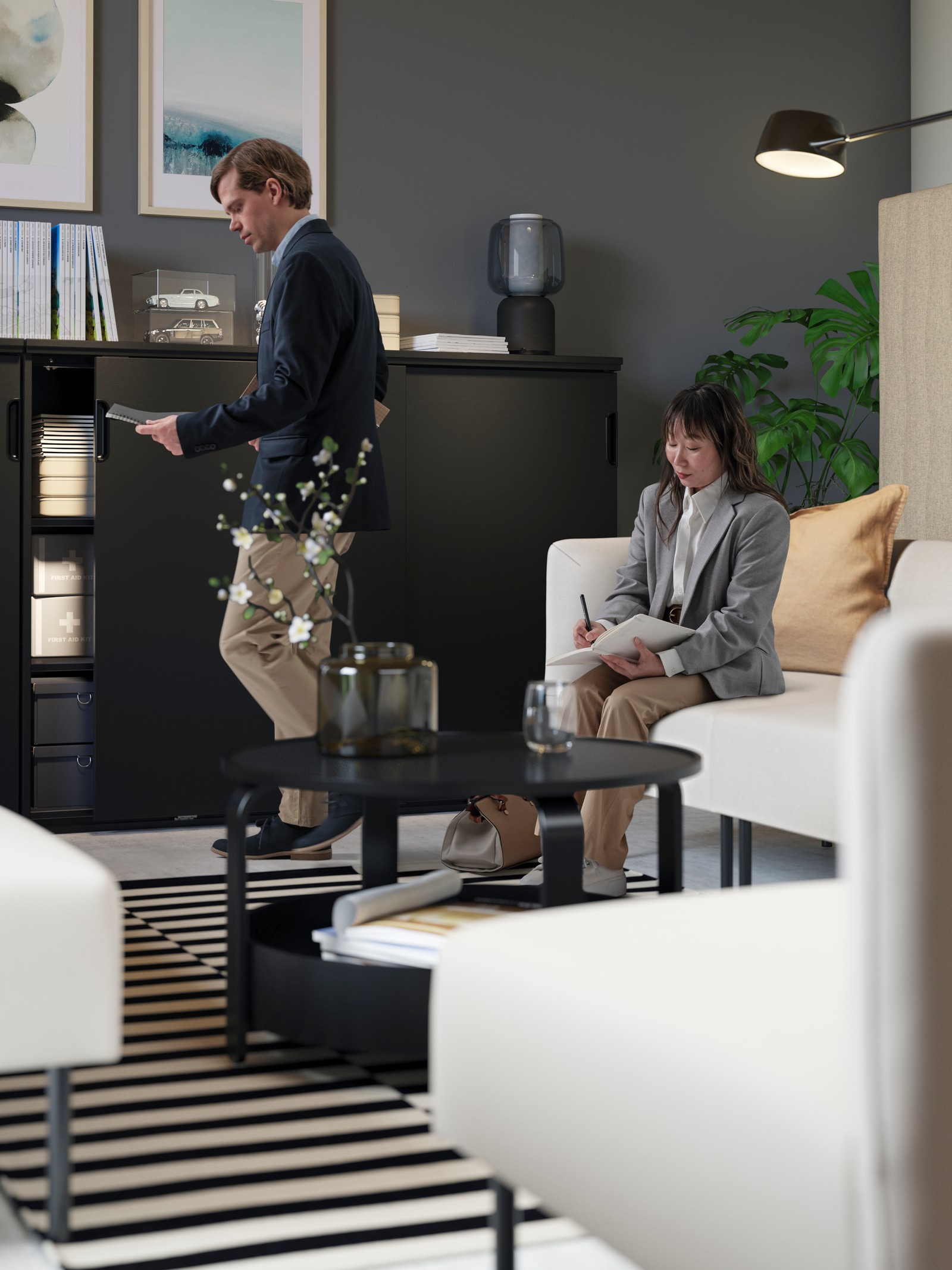 A lounge area with LILLEHEM beige modules, a black round BORGEBY coffee table and GALANT storage. A man and a woman are working.