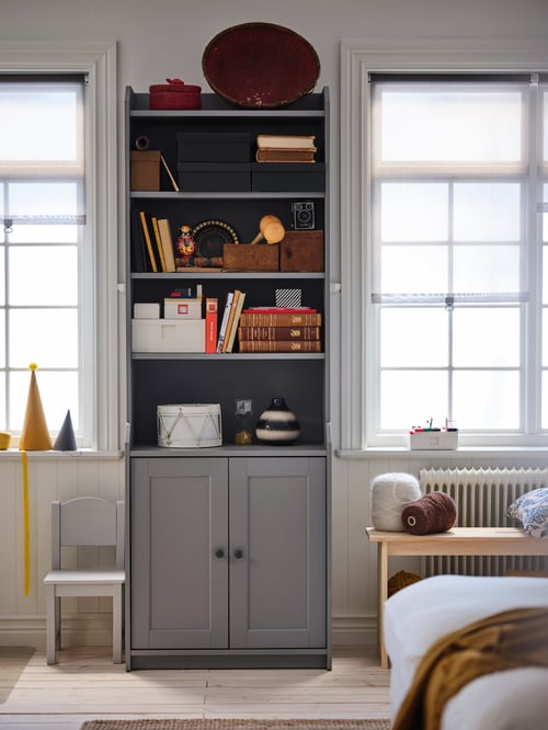 A children's room featuring a high cabinet with two doors, a children's chair, a bench with storage, and a Lego brick set.