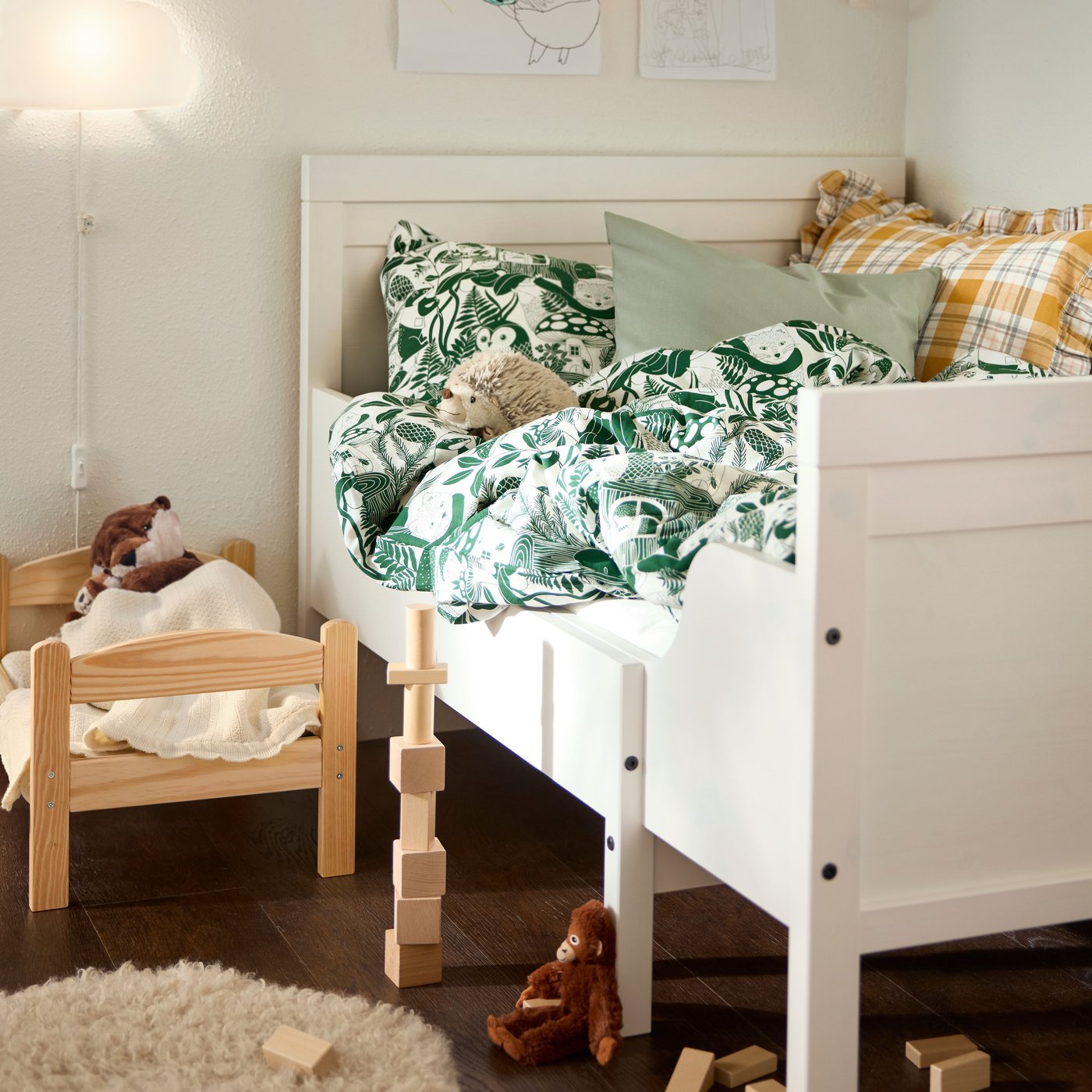 Es ist die Kinderecke mit einem ausziehbaren SUNDVIK Bettgestell, Kissen, Spielzeug und Papierdekorationen an der Wand zu sehen.