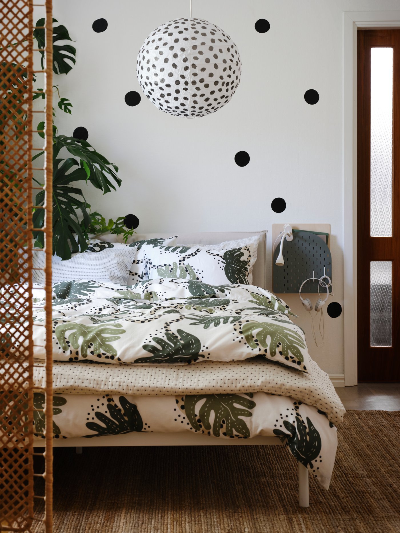 Una cama doble IKEA con un cubrelecho con diseño de plantas en un dormitorio de tonos blancos.