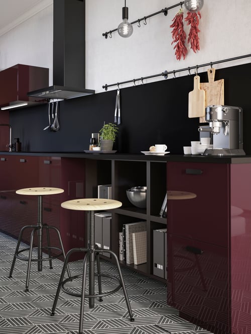 Two KULLABERG stools in pine/black are by a countertop in a burgundy kitchen. A coffee machine and some mugs are on top.