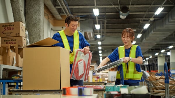 倉庫内でコワーカーが蛍光ベストを着て段ボールに商品を詰める。イケアの配送と受取りサービスの作業風景。