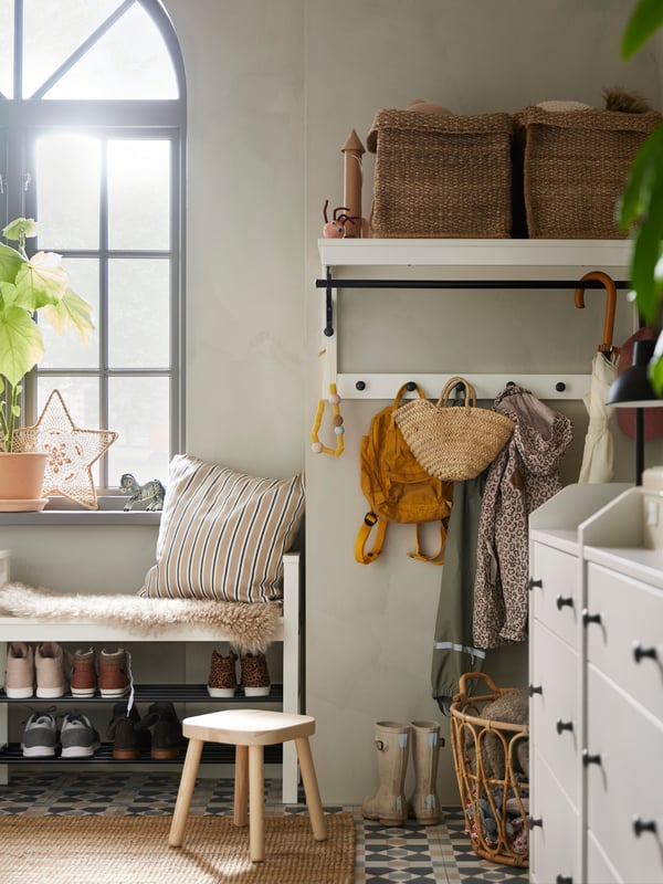 Two white HAUGA chests of 3 drawers stand in a hallway near two TJILLEVIPS baskets on a HEMNES hat rack attached to a wall.