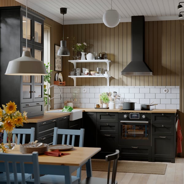 A kitchen with a black STENABY true fan oven is positioned beneath a sleek extractor hood, surrounded by cabinets and a sink.