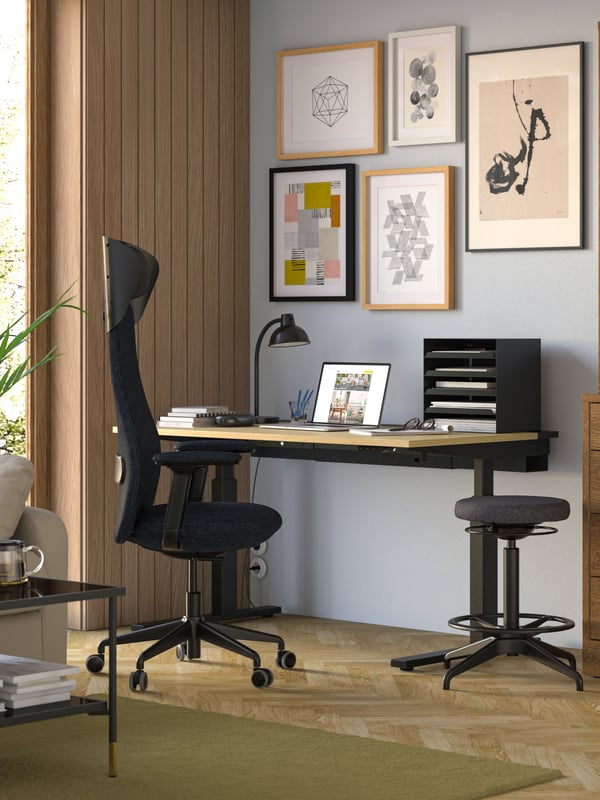 Een werkplek met een MITTZON bureau en een zwarte bureaustoel tegen een lichte muur aan met RÖDALM fotolijsten aan de wand.