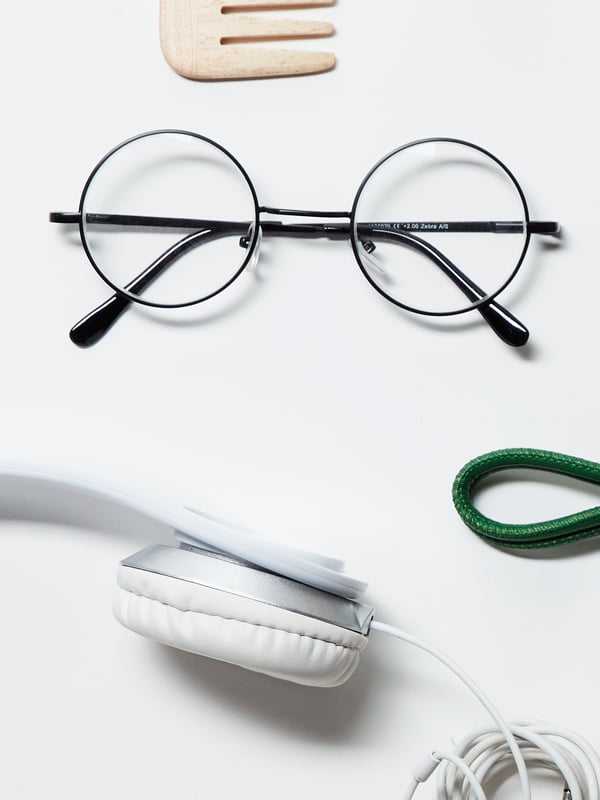 The bottom part of a comb, a pair of spectacles and part of a pair of headphones. Part of a larger image of everyday items.