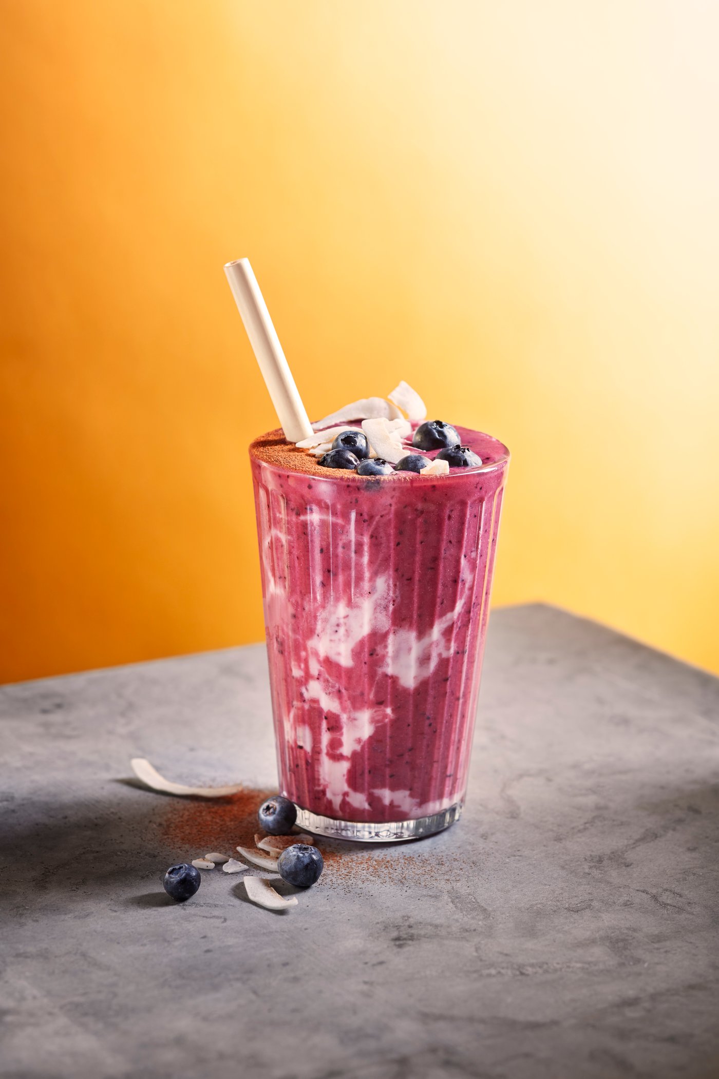 Un got que conté un batut de remolatxa i llet de civada de color rosa i blanc, amb una palleta. Està decorat amb nabius i flocs de coco.