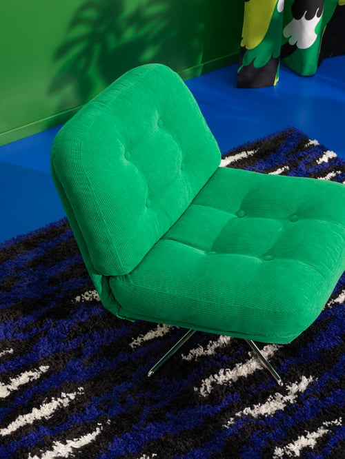 Fotoliu pivotant DYVLINGE verde așezat pe un covor BULLERREMSA cu grămadă mare, cu un model negru, alb și albastru.