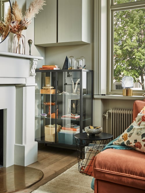 Living room with a grey glass door cabinet made of steel and tempered glass, placed under a cabinet next to a storage table.