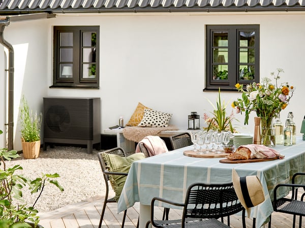Ein Haus von außen, davor steht ein Tisch mit Stühlen und an der Wand ist eine Luft-Wasser Wärmepumpe zu sehen.