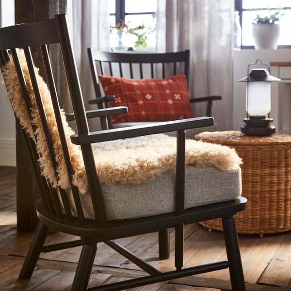 Una poltrona PERSBOL con sopra un tappeto SVINDINGE beige accanto a un pouf con contenitore TOLKNING.