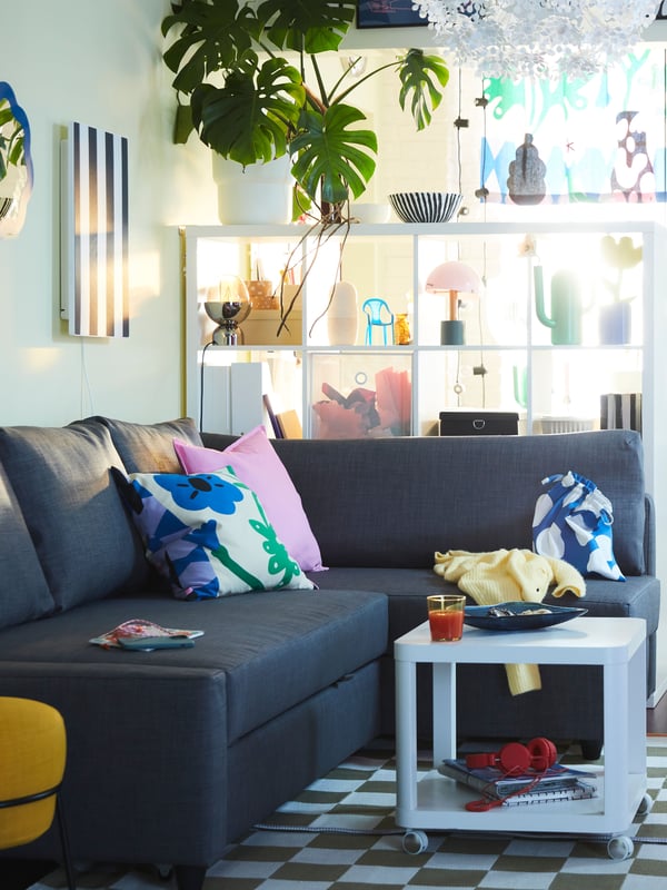 IKEA FRIHETEN grey sofa bed with bright coloured sofa cushions in a light green room with a checkered rug