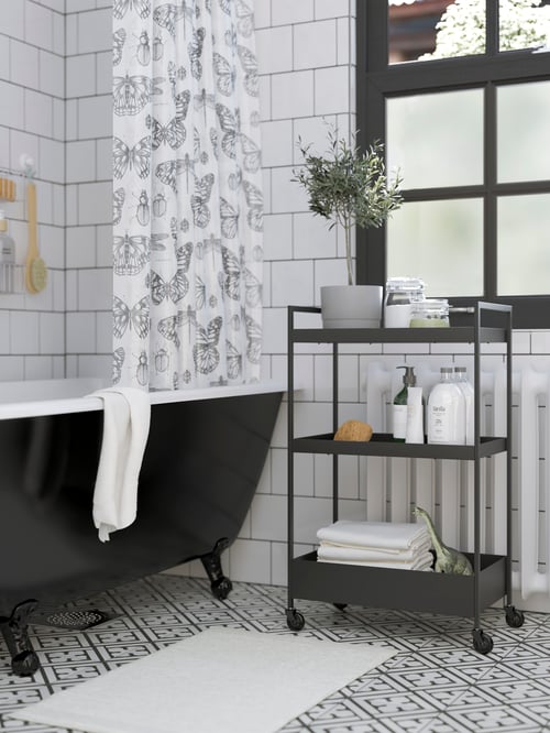 Baie scandinavă modernă cu cărucior metalic negru minimalist cu 3 rafturi, lângă o cadă alb-negru.