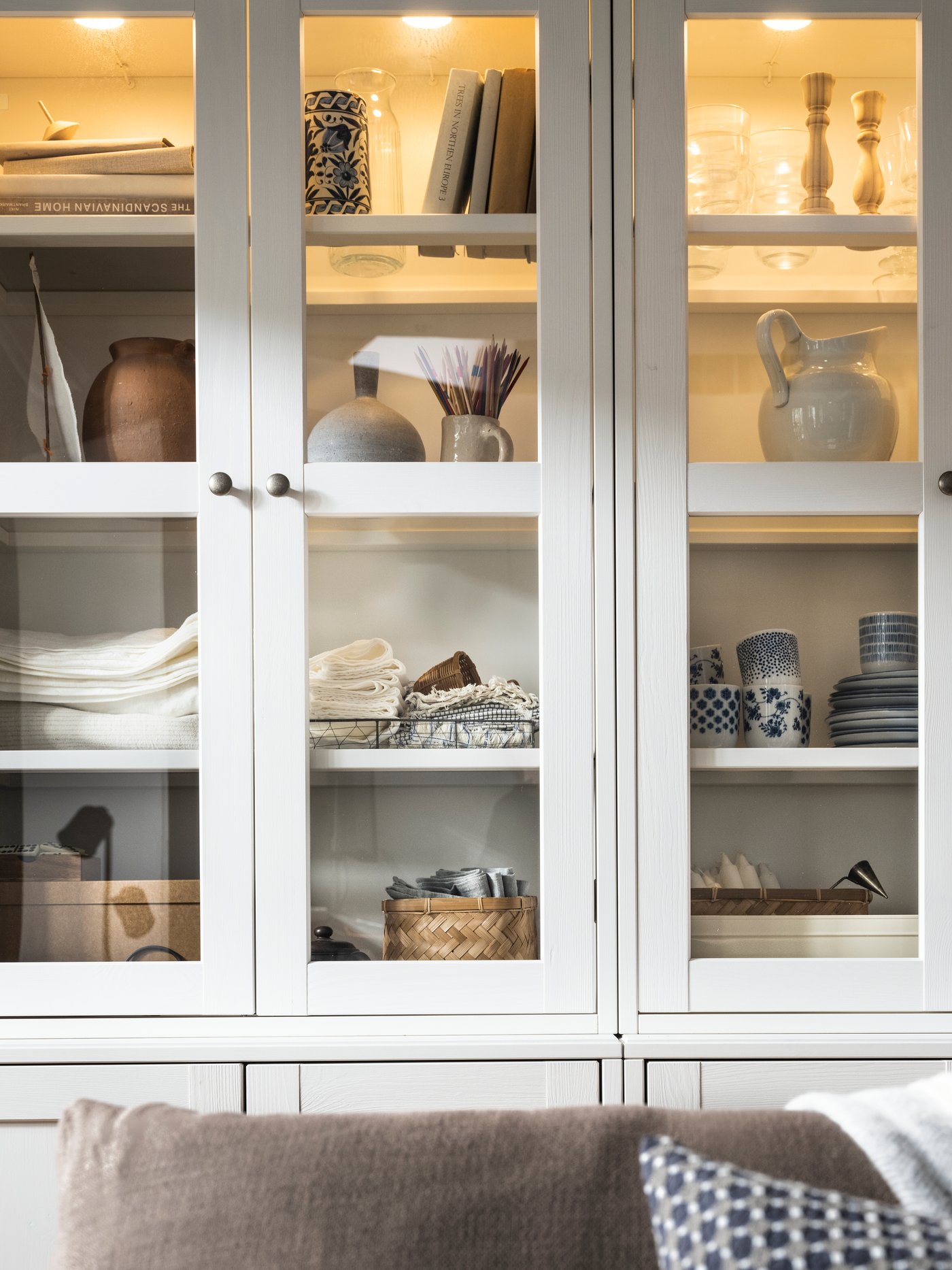 STRIMSÄV LED spotlights are mounted inside HAVSTA storage combinations with glass-doors with many objects on their shelves.