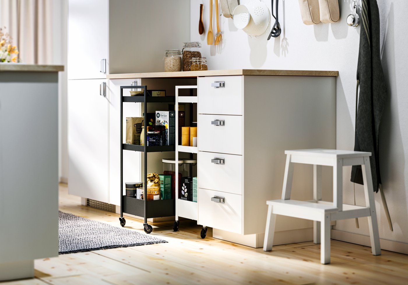 Una cucina con mobili base METOD bianchi e interni MAXIMERA, un piano di lavoro ERBACKEN e due carrelli NISSAFORS.