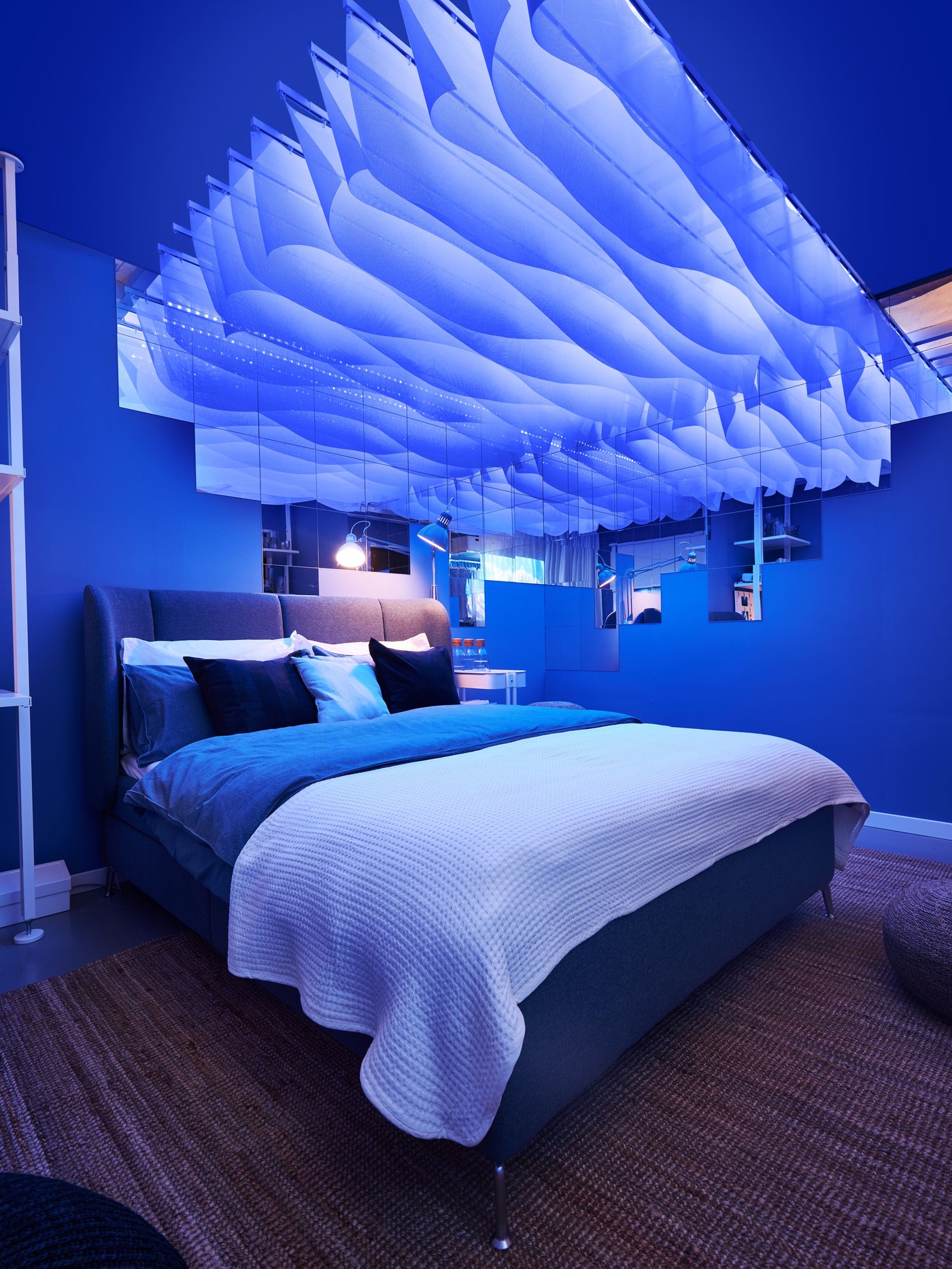A view of a bed in a room with a blue lighting. There are hanging cut curtains above the bed creating calm atmosphere.