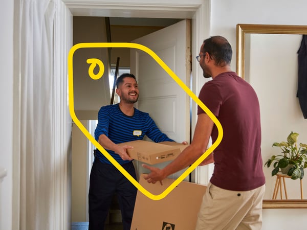En smilende fragtmand overrækker pakker til en mand i en entre.