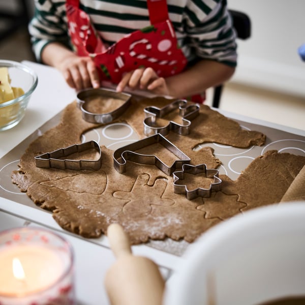 Et barn bruker VINTERFINT kakeskjærere til å skjære ut julefigurer av en utkjevlet pepperkakedeig.