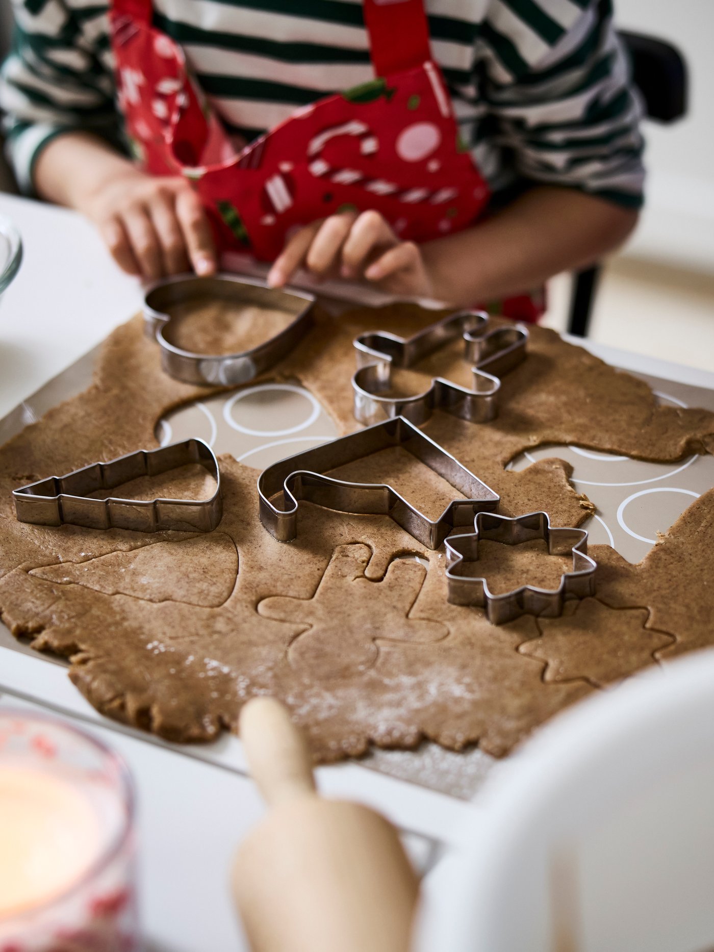 A child is using VINTERFINT pastry cutters to make festive cookie shapes from a flattened gingerbread dough.