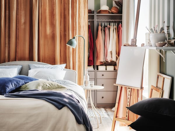 A beige RAMNEFJÄLL bed with a dark beige DYTÅG curtain behind it and a natural/unbleached cotton INDIRA bedspread on top.