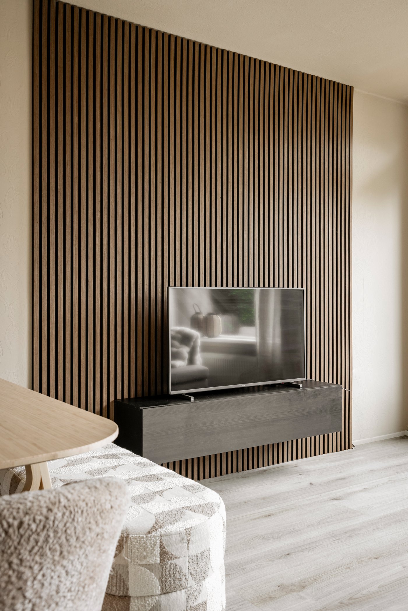 Een muur met houten wandpaneel, waaraan een tv-meubel hangt met daarop een tv.