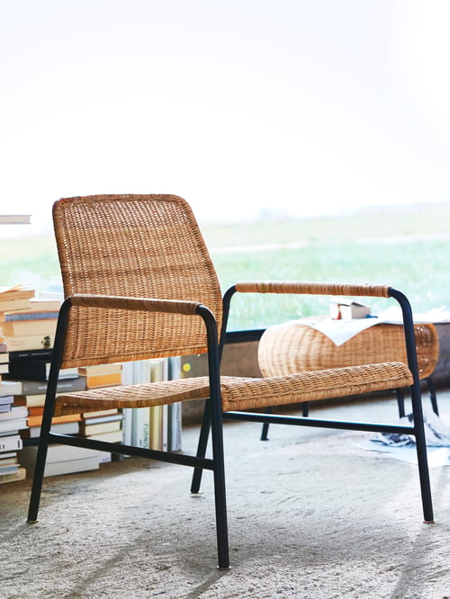 ULRISKBERG Sessel aus Rattan mit Beinen in Anthrazit neben einem Bücherstapel und einem Fenster.