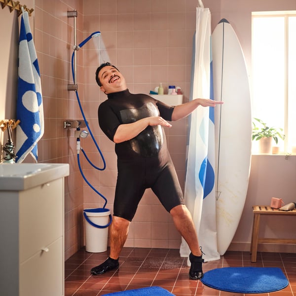 A person in a wetsuit is dancing in the shower with water spraying from a BERGVATTNET single hand spray shower with hose.
