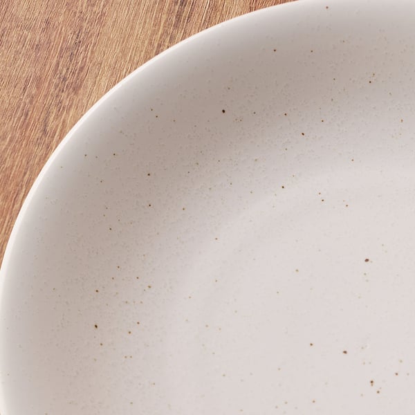 木製のテーブルの上に置かれた、茶色い小さな斑点がある白い陶器のボウルの縁のクローズアップ。

