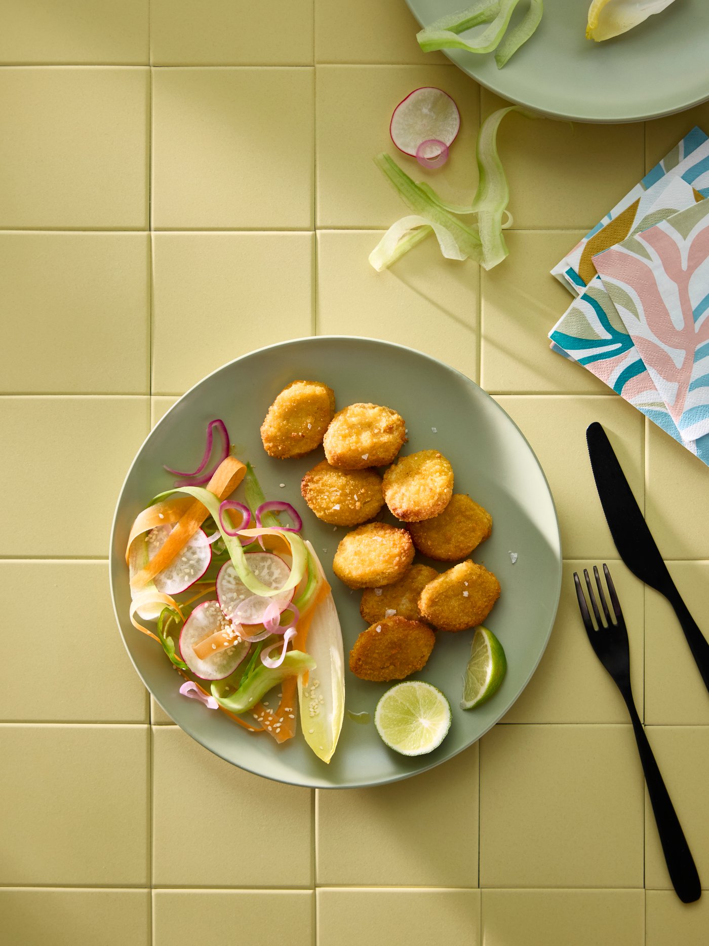 SLAGVERK wheat-based pieces and a fresh vegetable sallad on a green FÄRGKLAR plate with TILLAGD knife and fork next to it.