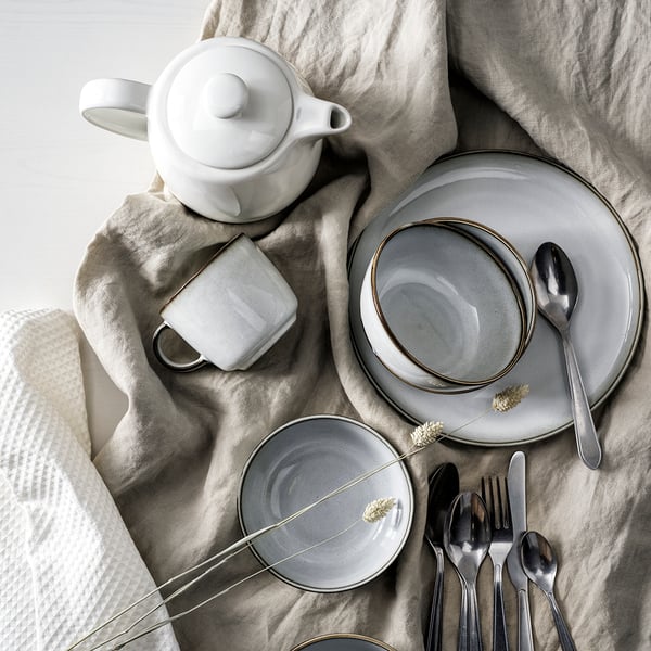 GLADELIG bowls, plates, VARDAGEN off white pot and cutlery flat lay atop a cloth. 