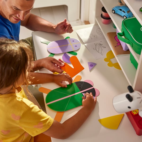 A child and an adult sitting together at a children’s desk assemble colourful GRESIMOJS decoration in a child’s room.