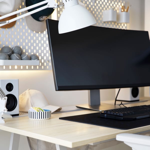A smart, wireless ORMANÄS lighting strip glows through the holes and of white SKÅDIS pegboards on a wall behind a desk.