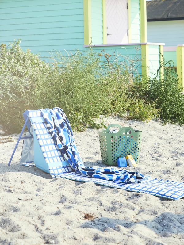 STRANDÖN sun lounger in blue and white set up on the beach with a towel on top, ready for you to relax and enjoy the sunshine.