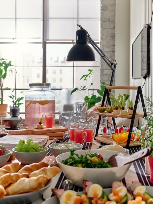 A modern kitchen that features a serving tray, a serving bowl, a chopping board, a work lamp, and a tray with 3 bowls.