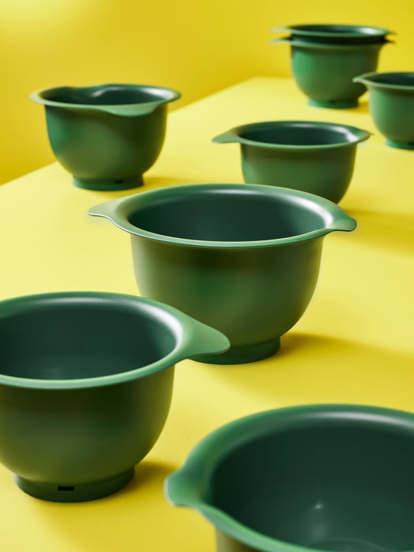 Eight green VISPAD mixing bowls are scattered around a yellow tabletop in a bright yellow room.