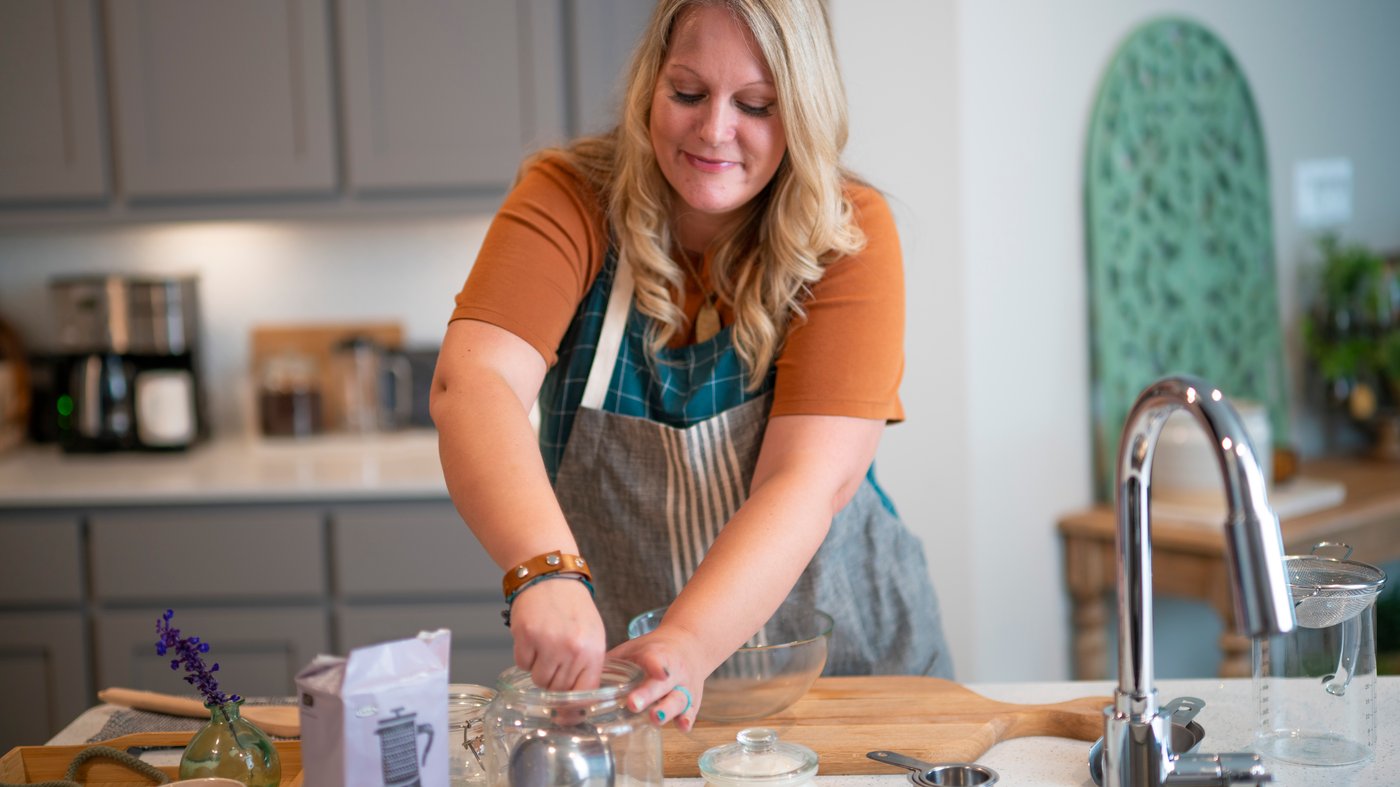 Woman preparing a homemade scrub mix in the kitchen, mixing PÅTÅR press coffee and honey in a KORKEN jar.