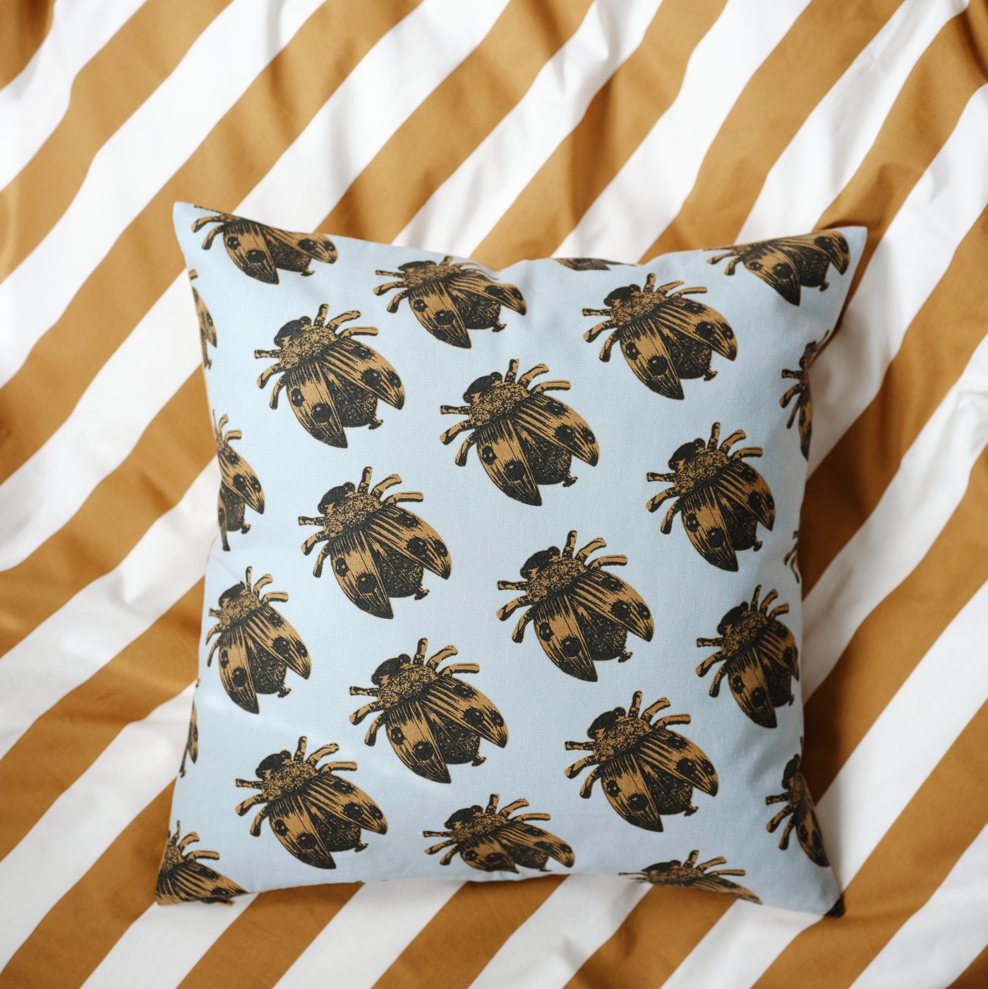 A NÄBBSPINNARE cushion cover with a fun insect print in dark yellow/pale blue, on top of a striped ÄNGLATRUMPET duvet cover.