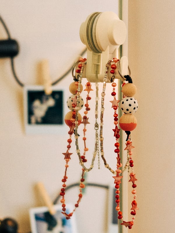 A close-up of a chunky wooden necklace hanging on a TISKEN hook put on a mirror using the suction cup.