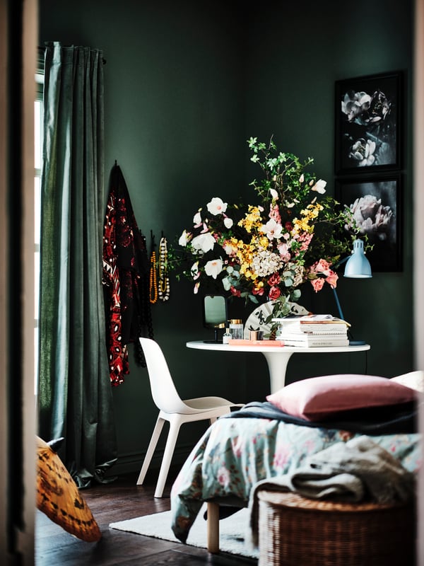 A corner of a bedroom with an ODGER chair and a white/white DOCKSTA table with a large display of SMYCKA artificial flowers.