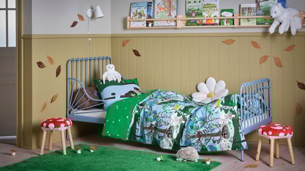 A grey-blue MINNEN extendable bed with SKOGSDUVA bed linen. On the floor lies a green SKOGSDUVA high-pile rug.