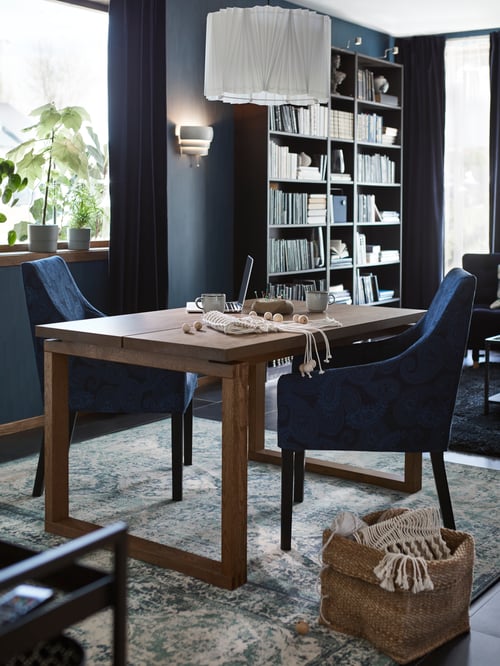 Ein MÖRBYLÅNGA Tisch mit zwei blauen Essstühlen. Auf dem Tisch stehen ein Laptop und Bastelmaterial, von oben hängt eine Hängeleuchte herab.