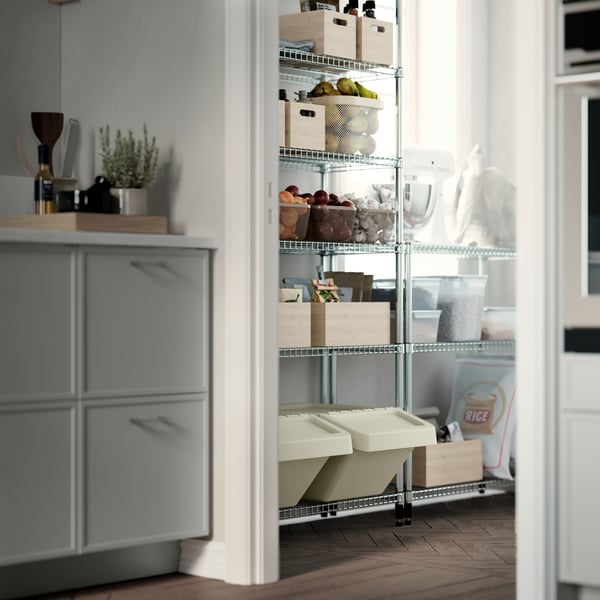 Kitchen corner next to a pantry shelving unit with storage boxes, baskets and waste sorting bins.