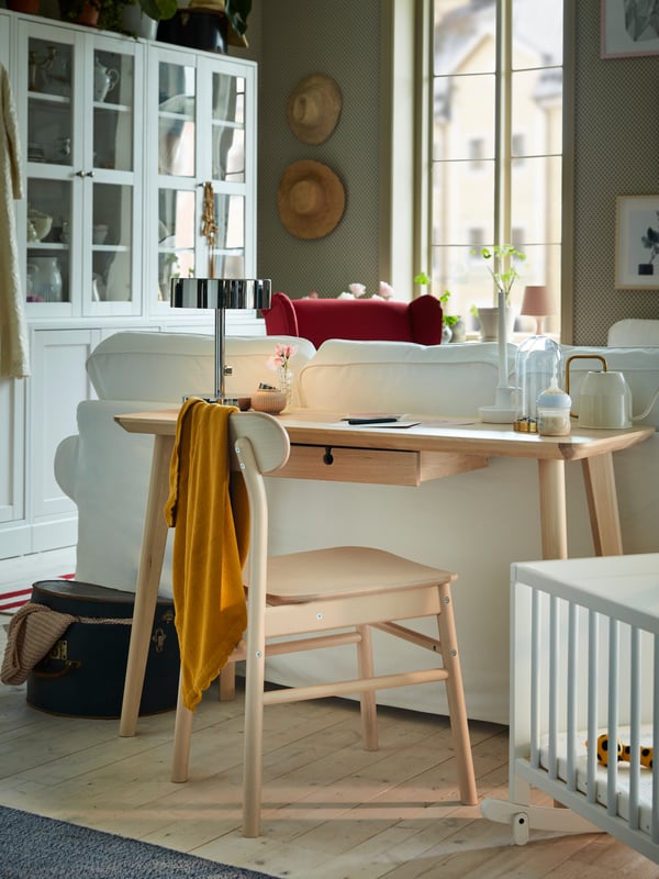 A desk in ash veneer is standing behind an EKTORP sofa, and the desk provides a workspace in a living room.