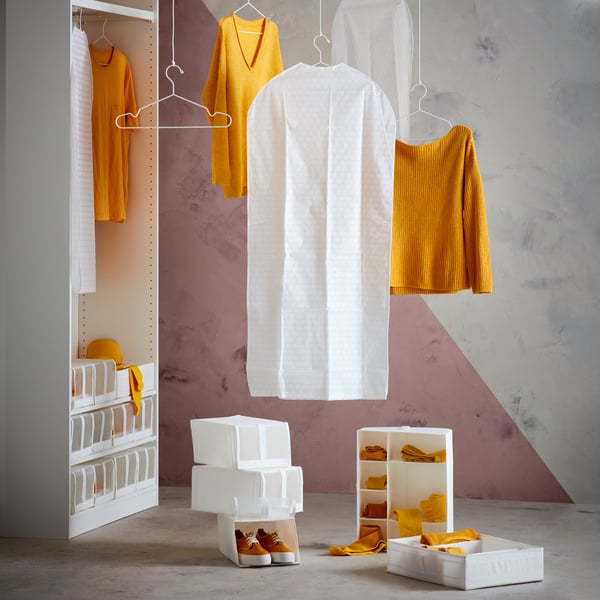 White SKUBB organisers and shoeboxes and yellow garments on hangers artfully arranged in and next to a doorless PAX wardrobe.